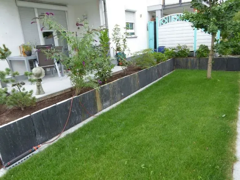 Ein üppig grüner Garten mit einem Zaun und einer Terrasse im Hintergrund.