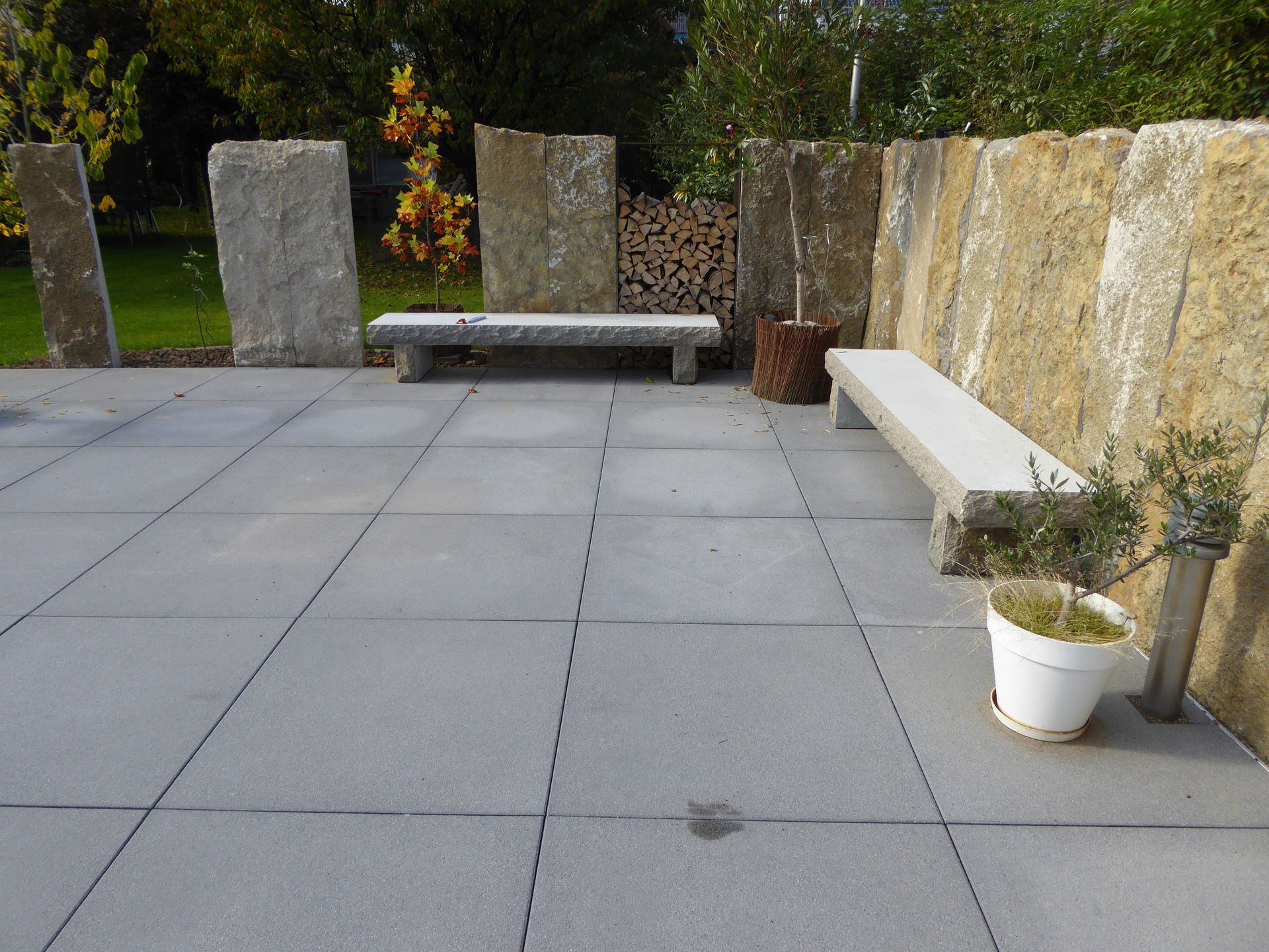 Steinterrasse mit Bänken, dekorativer Steinmauer und Topfpflanze.