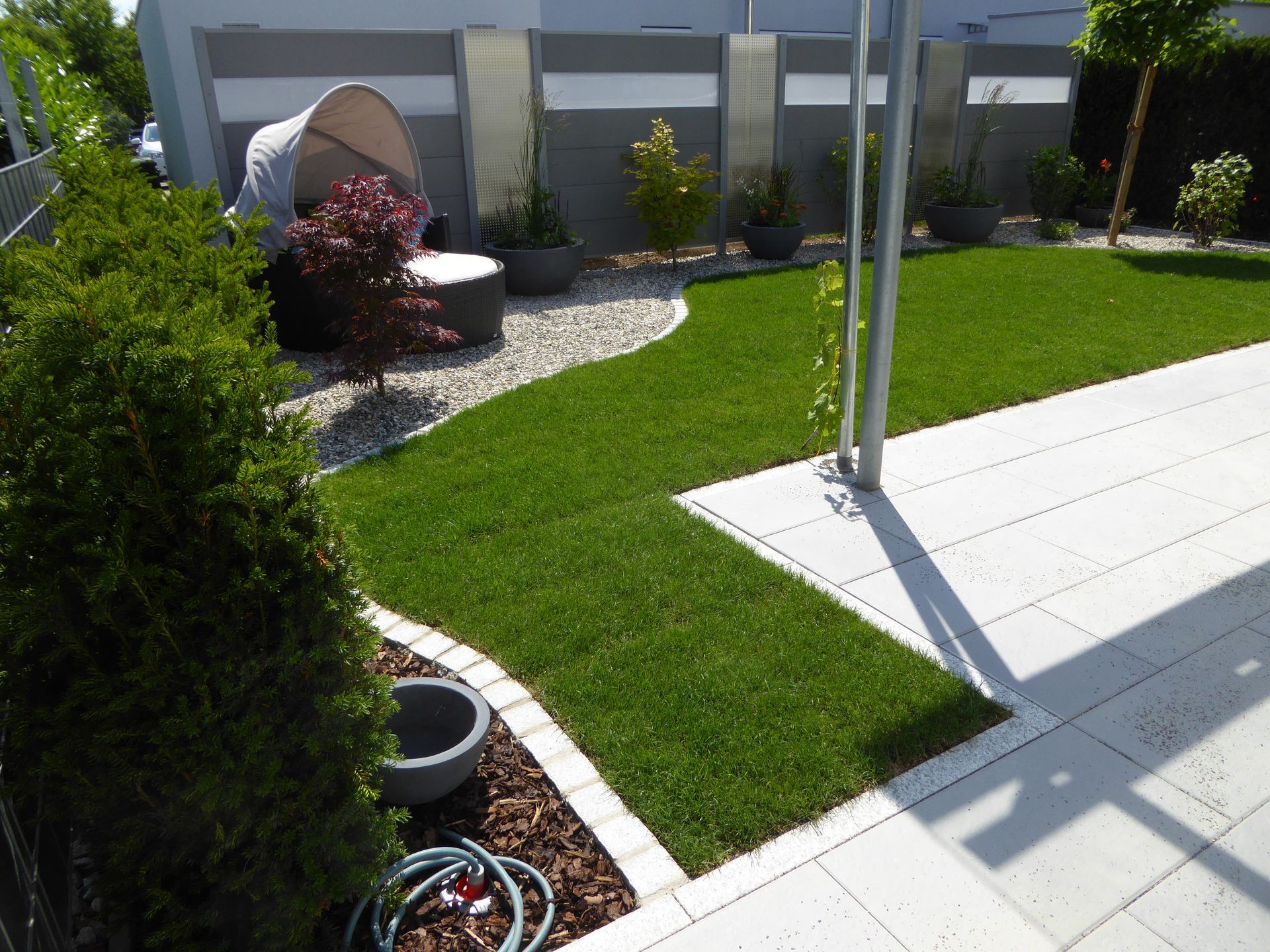 Ein gepflegter, grüner Rasen mit geschwungenem Rand grenzt an eine gepflasterte Terrasse.