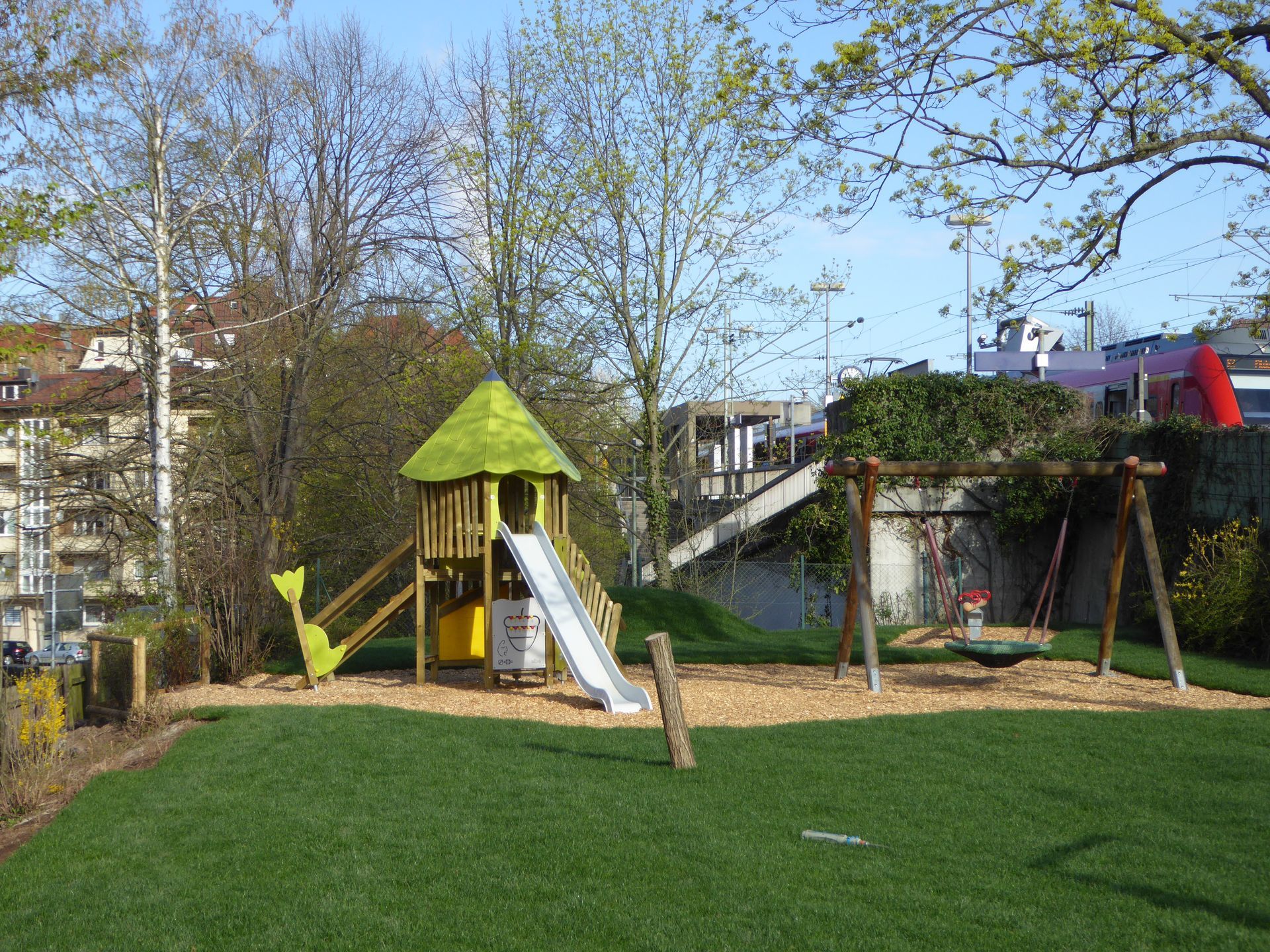Spielplatz mit Spielgerüsten aus Holz und Schaukeln auf grünem Rasen.