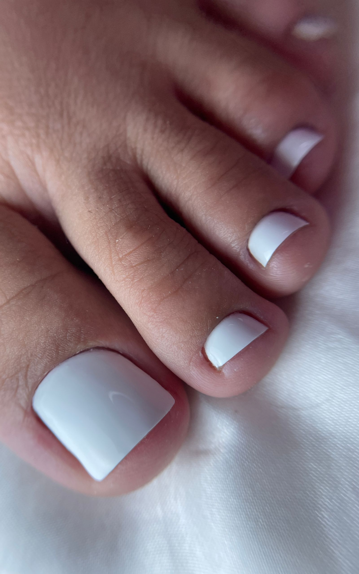 Una profesional de la belleza, vestida con una chaqueta beige y guantes, examina las uñas de una persona con camisa negra en un salón de belleza.
