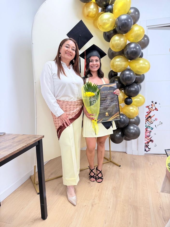 Cinco personas posando para una foto de graduación frente a un arco de globos, sosteniendo sus certificados en un evento de la academia.