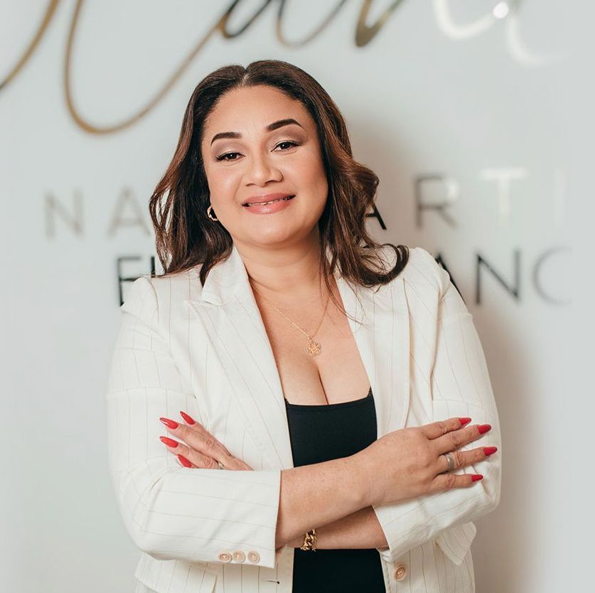 Una persona con chaqueta blanca y blusa negra sonríe con los brazos cruzados sobre un fondo con texto parcial.