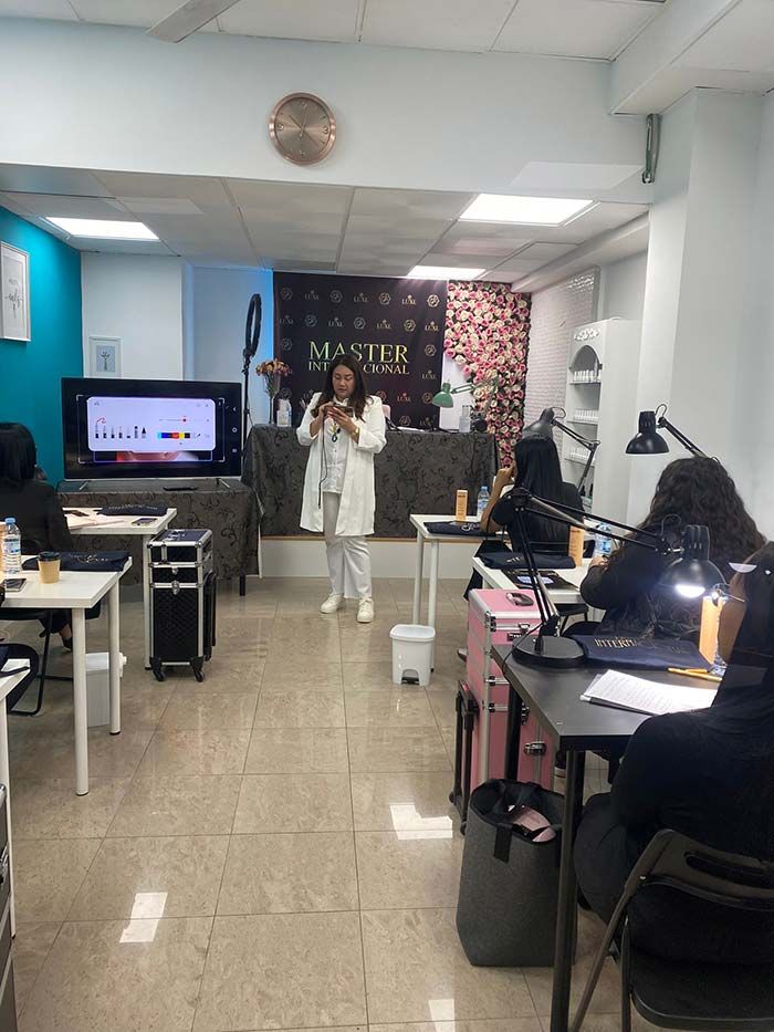 Un instructor con bata blanca se encuentra frente a un aula, presentando la información en una pantalla a los estudiantes ubicados en estaciones de trabajo individuales.