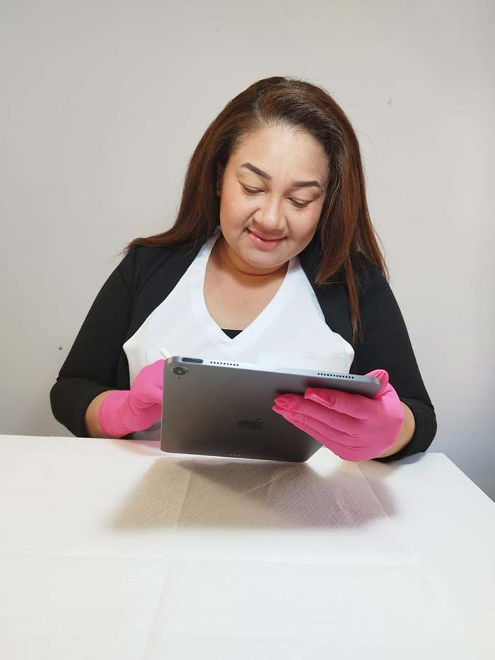Una persona con una blusa blanca, un blazer negro y guantes rosas sonríe mientras sostiene una tableta digital.