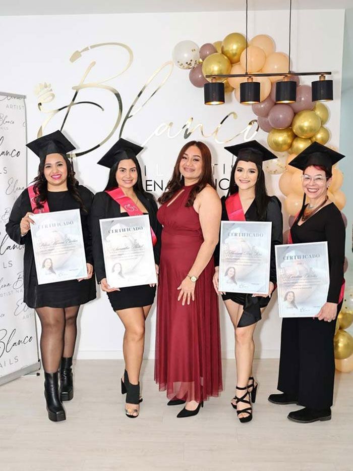 Cinco personas posando para una foto de graduación frente a un arco de globos, sosteniendo sus certificados en un evento de la academia.