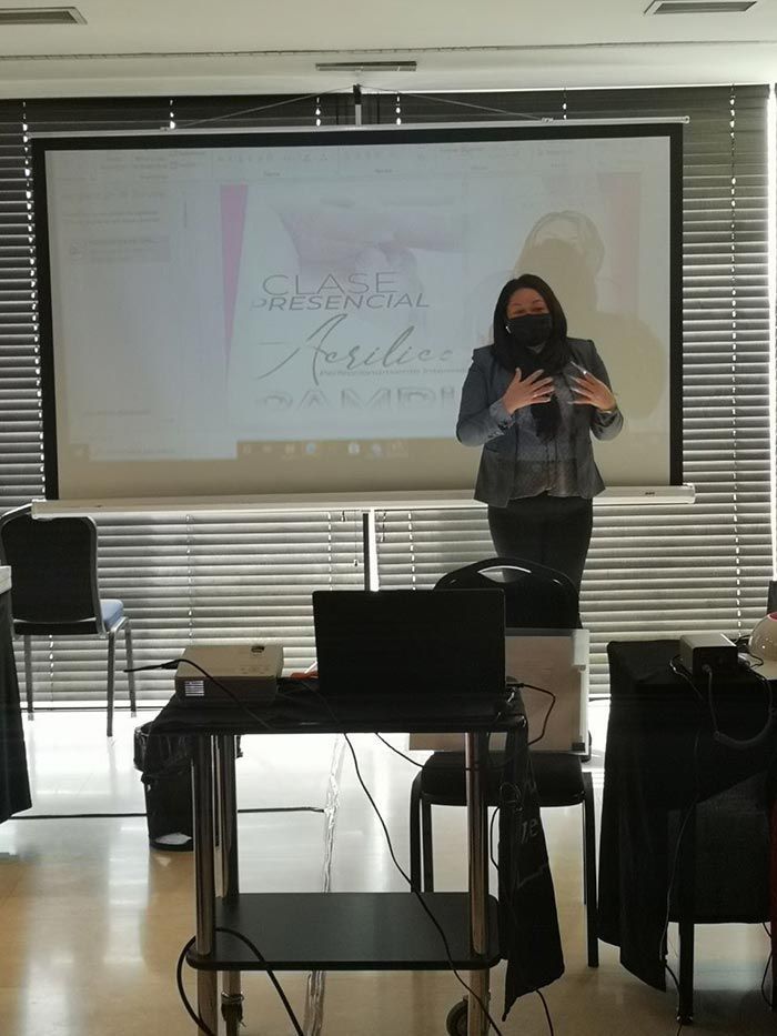 Un orador se sitúa frente a una pantalla de proyección que muestra texto en un aula, gesticulando con las manos levantadas.