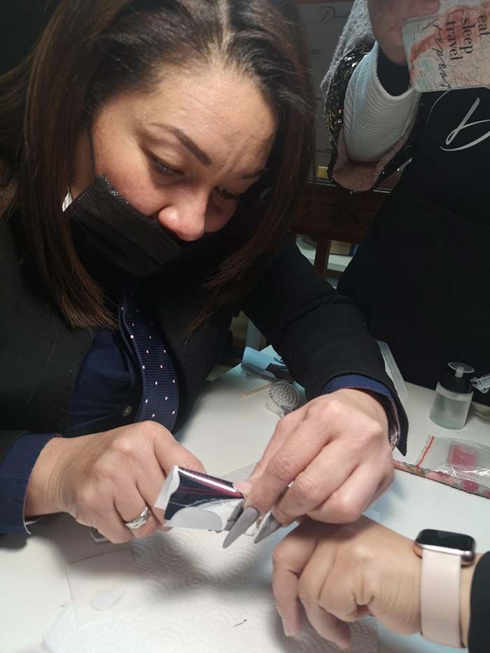 Una persona con mascarilla se concentraba en aplicar cuidadosamente una tira adhesiva para uñas sobre la uña larga y bien cuidada de una clienta.