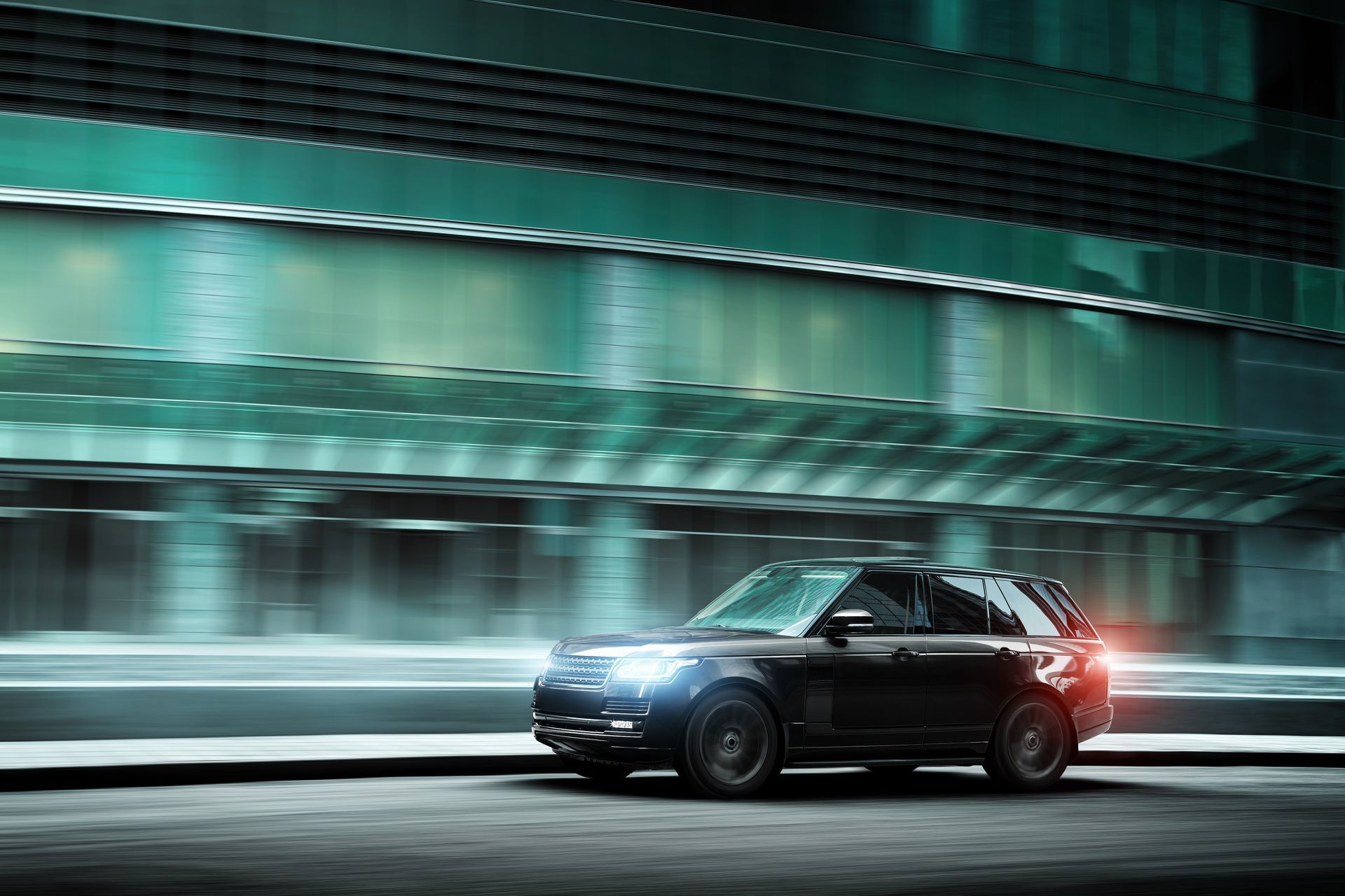 Un SUV noir passant à toute vitesse devant un bâtiment moderne de couleur bleu sarcelle la nuit.