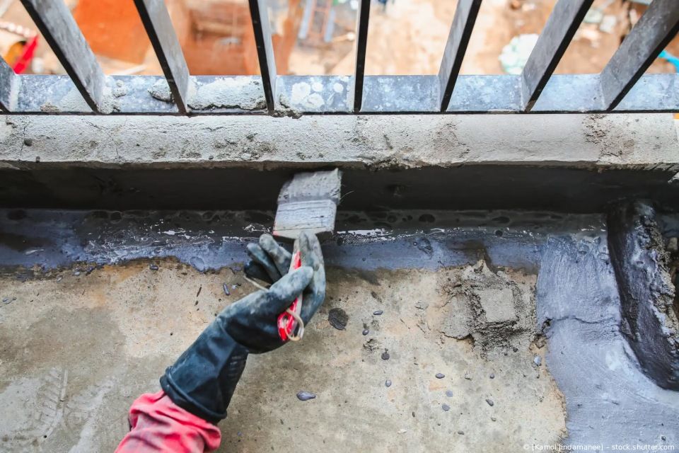 Eine Person benutzt eine Kelle, um rissigen Beton neben einem Metallgeländer im Freien auszubessern.
