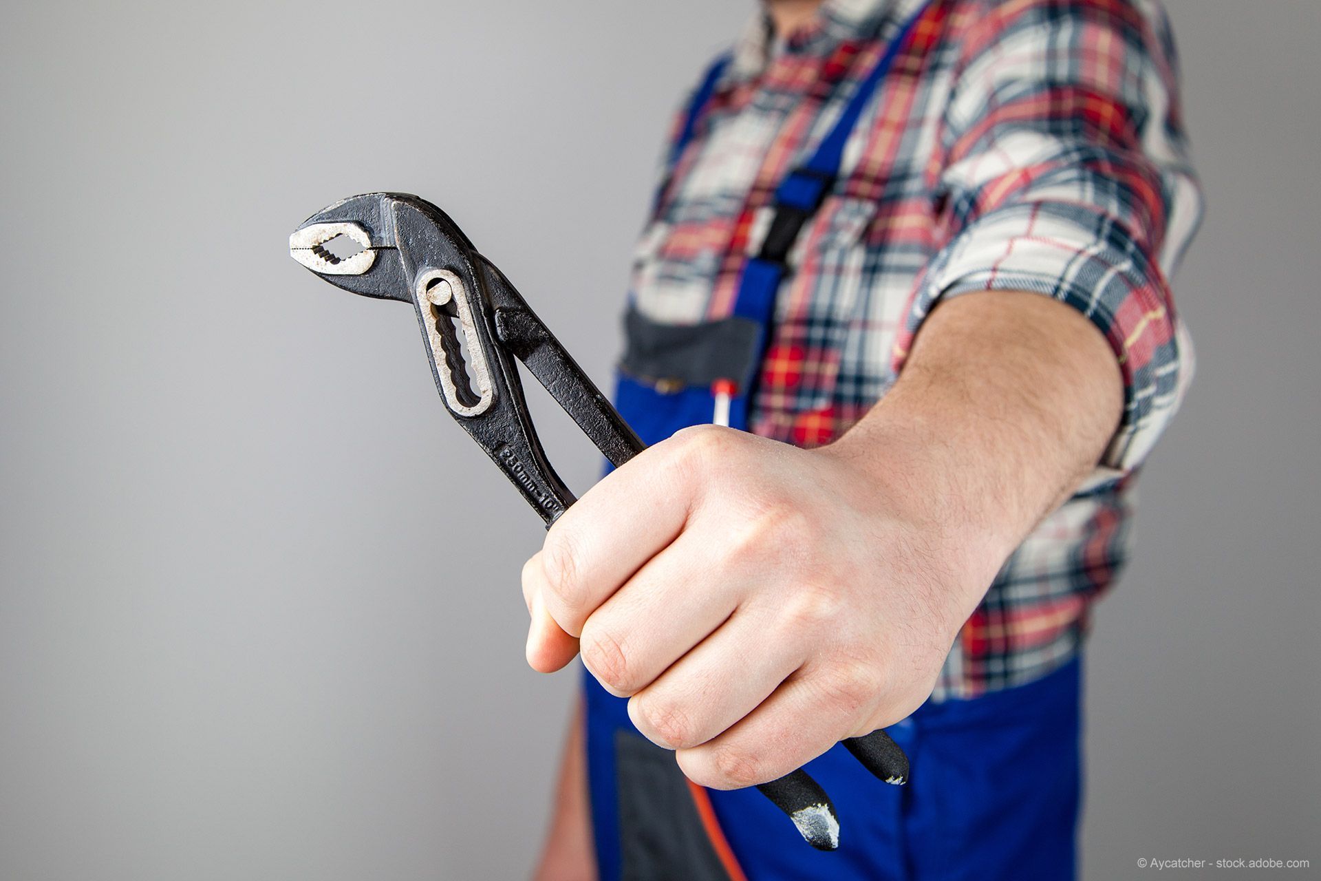 Handwerker in blauem Overall und kariertem Hemd hält eine verstellbare Zange.
