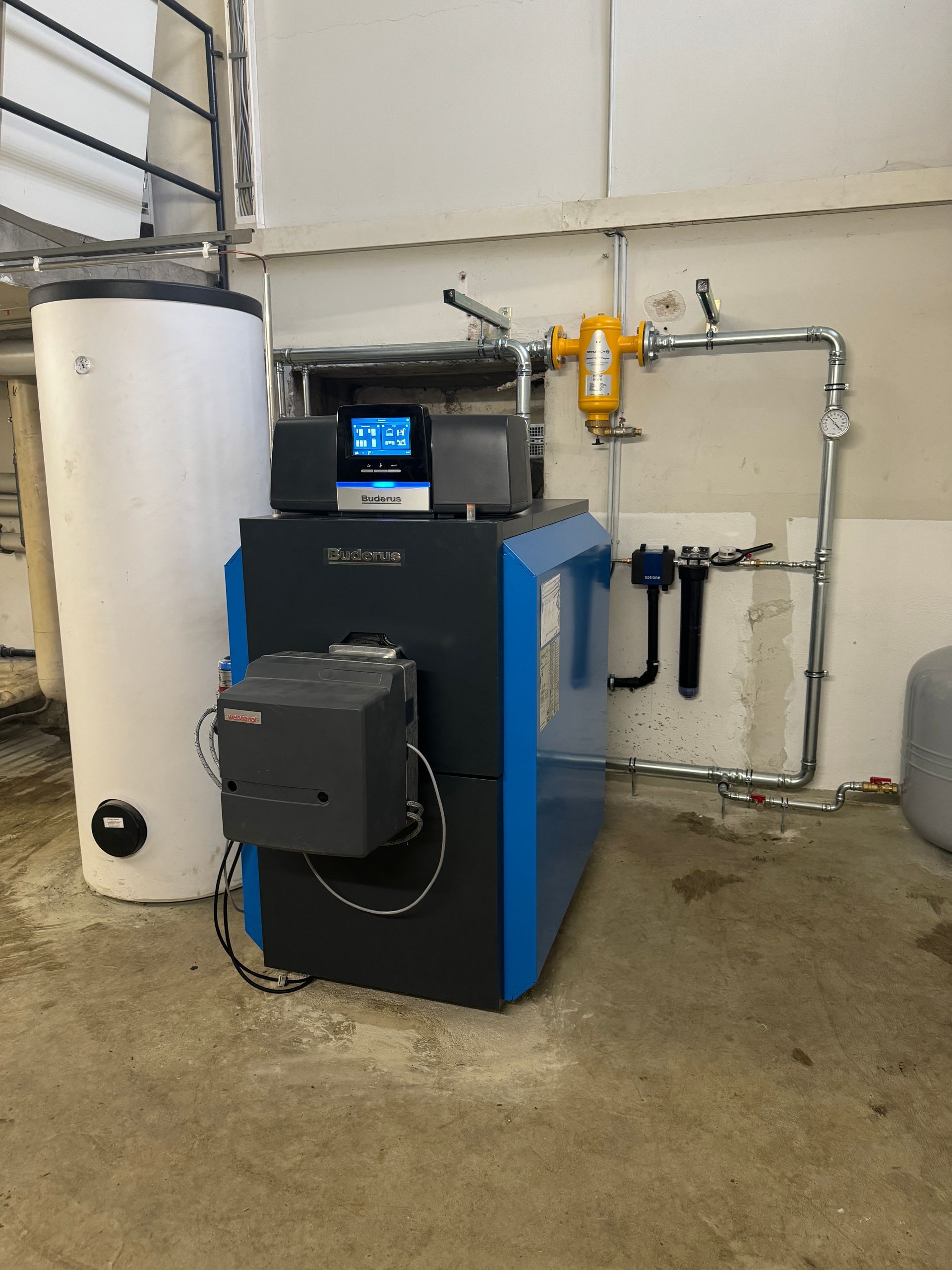 Blau-schwarzes Heizsystem mit weißem Wassertank in einem Hauswirtschaftsraum.