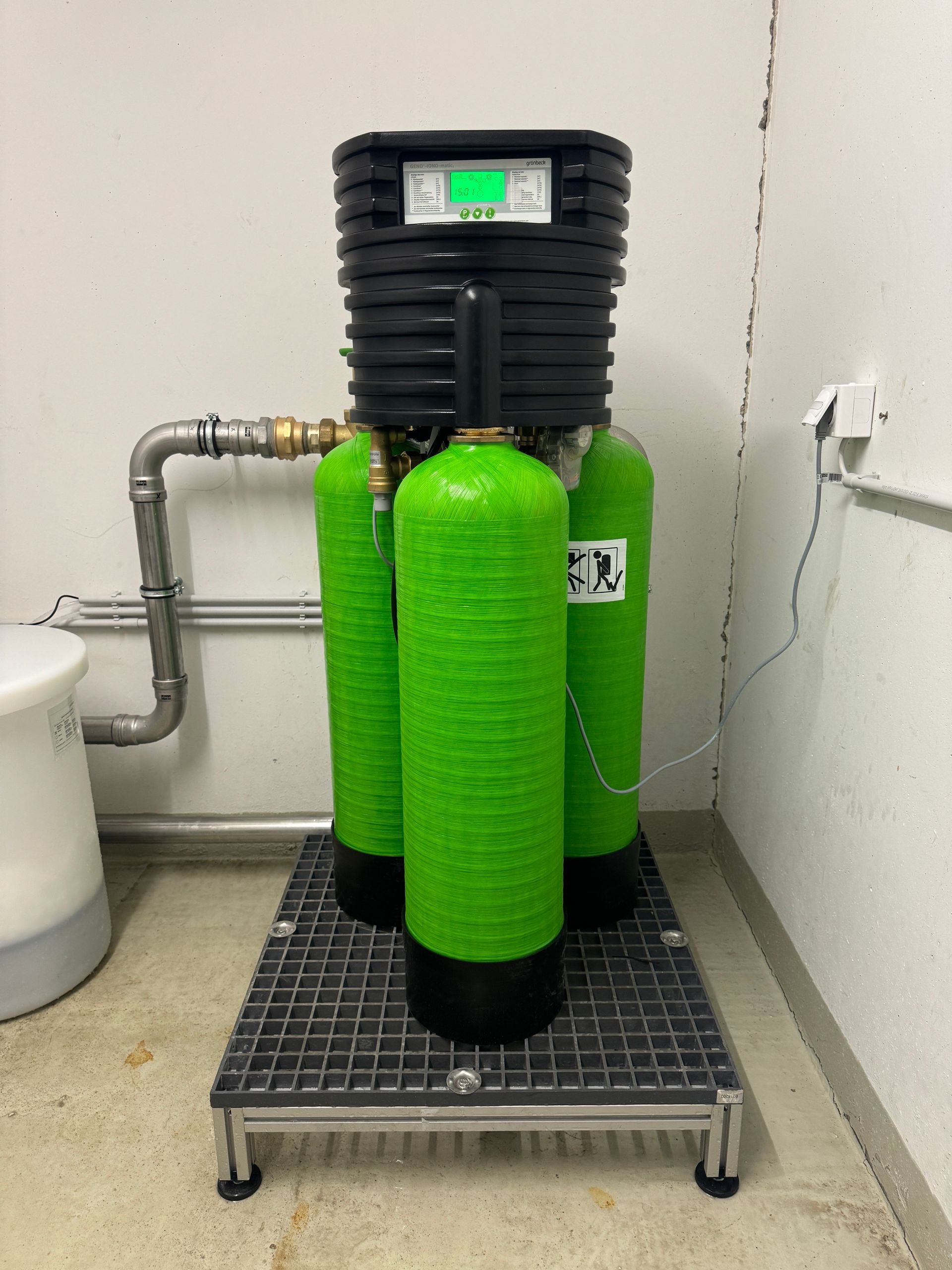 Grüne Gasflaschen mit schwarzer Steuereinheit auf einem Metallgestell vor einer weißen Wand.