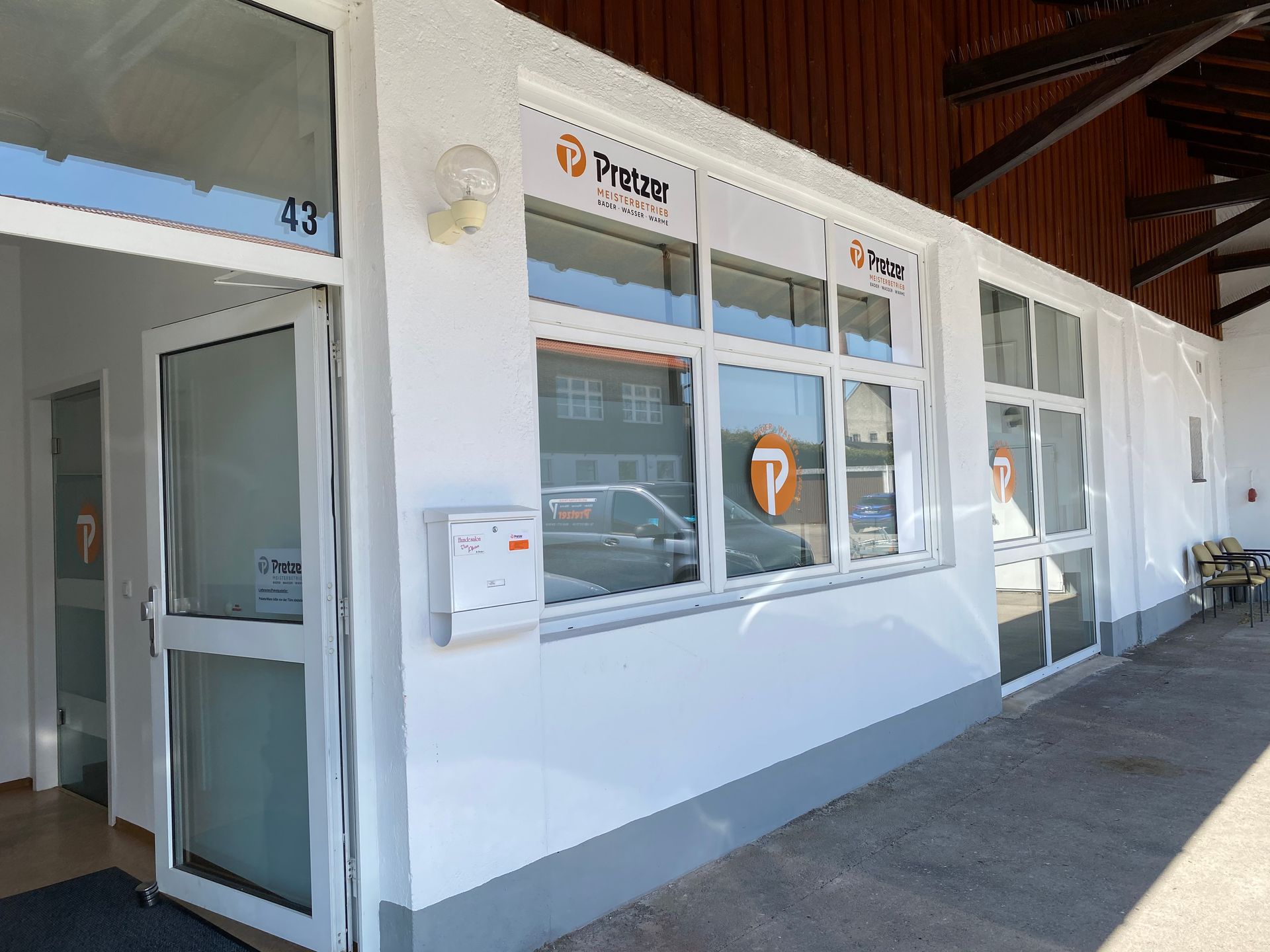 Landen der Firma Pretzer, weißes Gebäude mit Fenstern, einer Tür und dem Firmenlogo