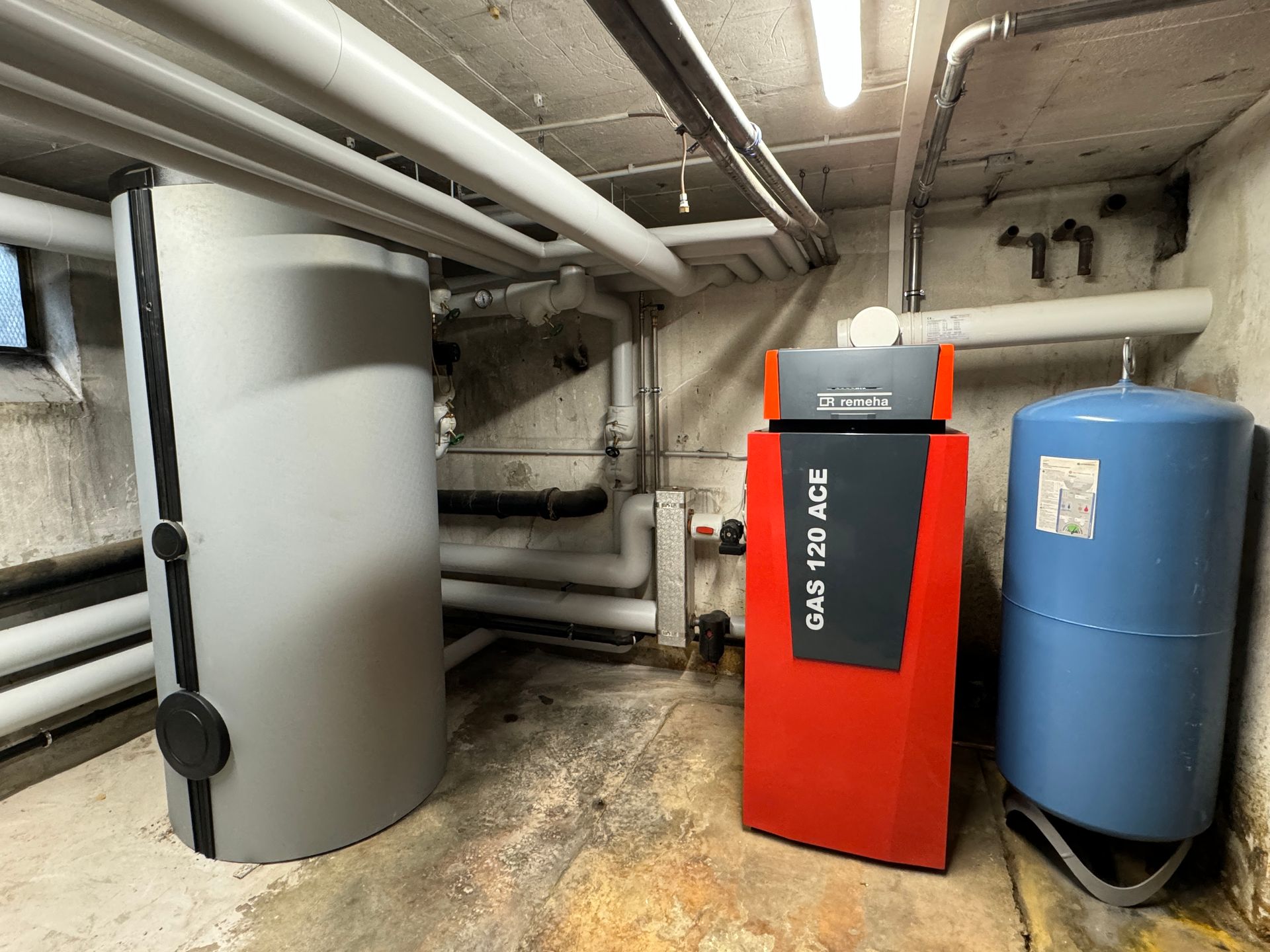 Keller mit Grauwassertank, roter Heizung, blauem Tank und Rohren.