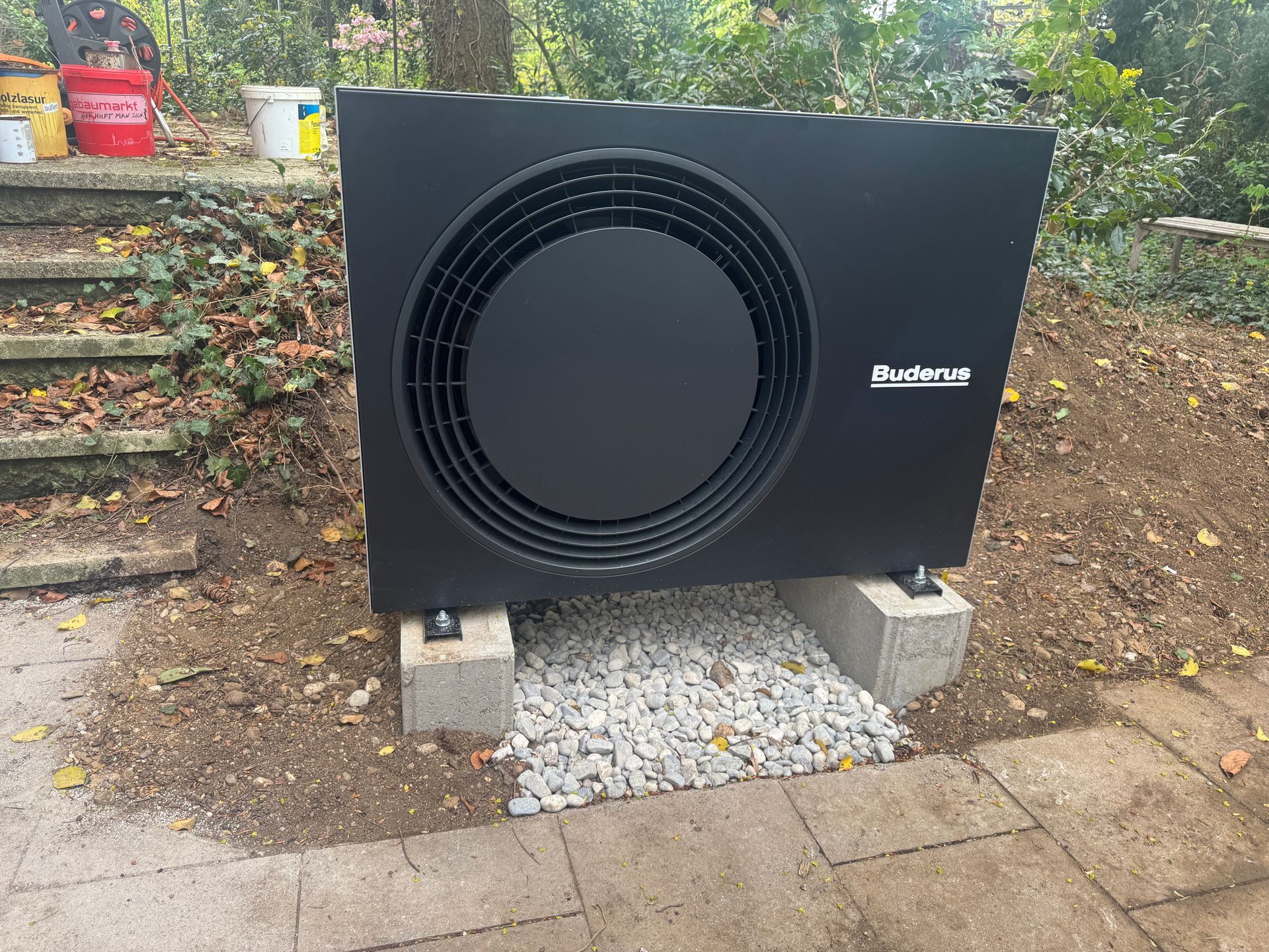 Schwarze Buderus Wärmepumpeneinheit auf Betonblöcken mit Kies, Außenaufstellung.