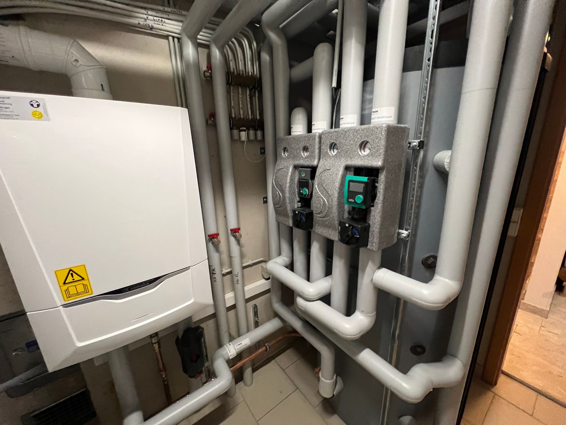 Weiße Rohre und Geräte im Hauswirtschaftsraum. Zwei Pumpen mit grünen Anzeigen, plus weißer Kasten auf der linken Seite.