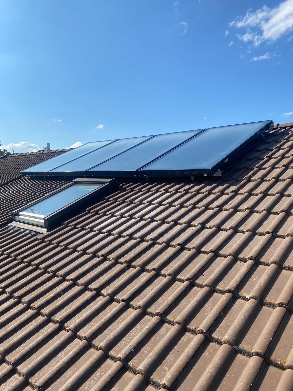 Solarmodule und Oberlicht auf einem braunen Ziegeldach vor blauem Himmel.