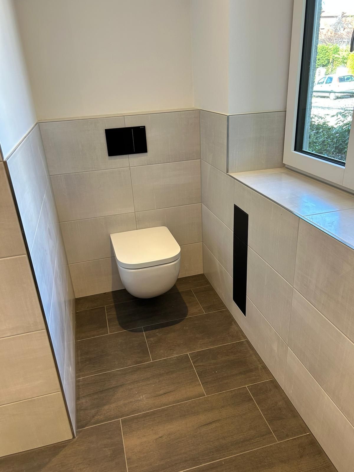 Badezimmer mit Wand-WC, schwarzer Spülplatte und Fenster.