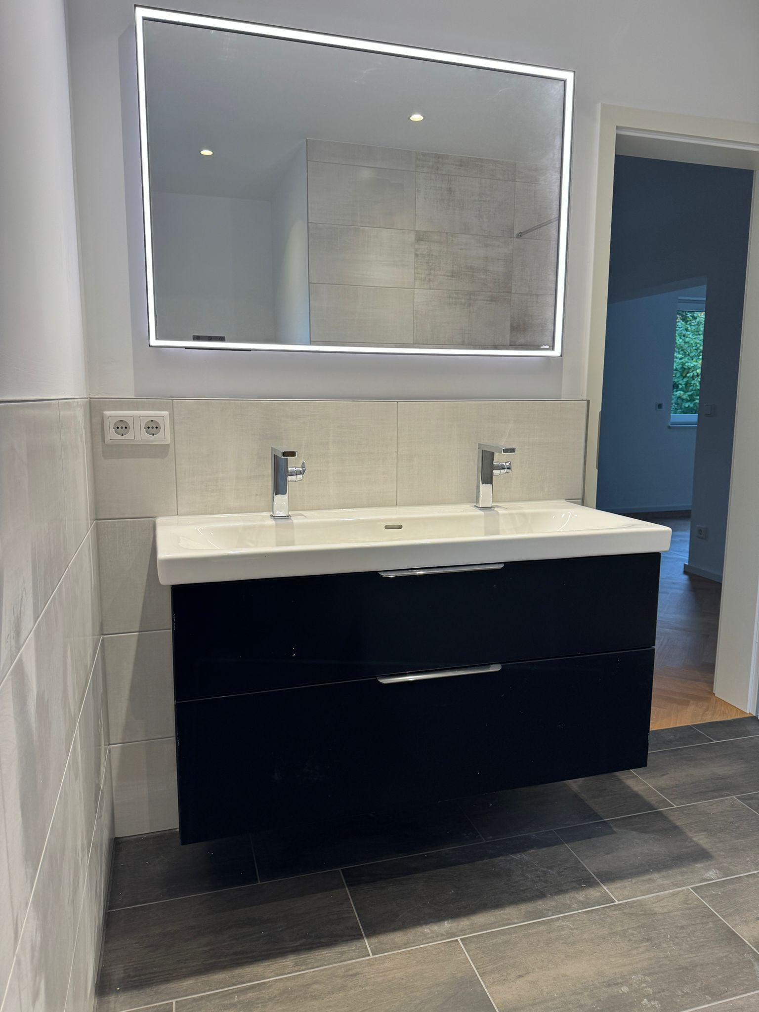 Modernes Badezimmer mit schwarzem Waschtisch, weißem Waschbecken, hinterleuchtetem Spiegel und Chromarmaturen.