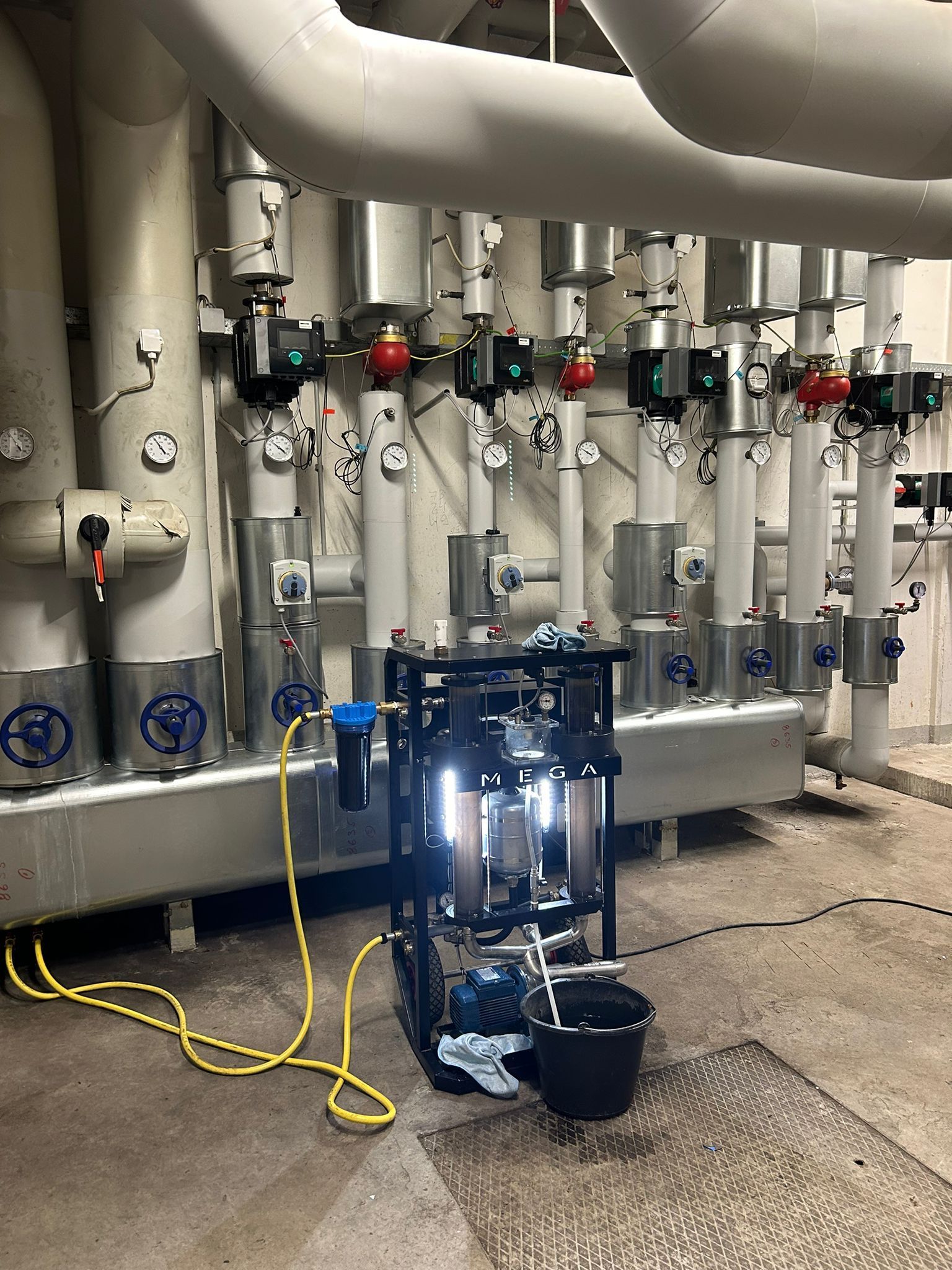 Schwarzer Wagen mit Ausrüstung in der Nähe von Industrierohren. Gelber Schlauch und Eimer auf dem Boden.