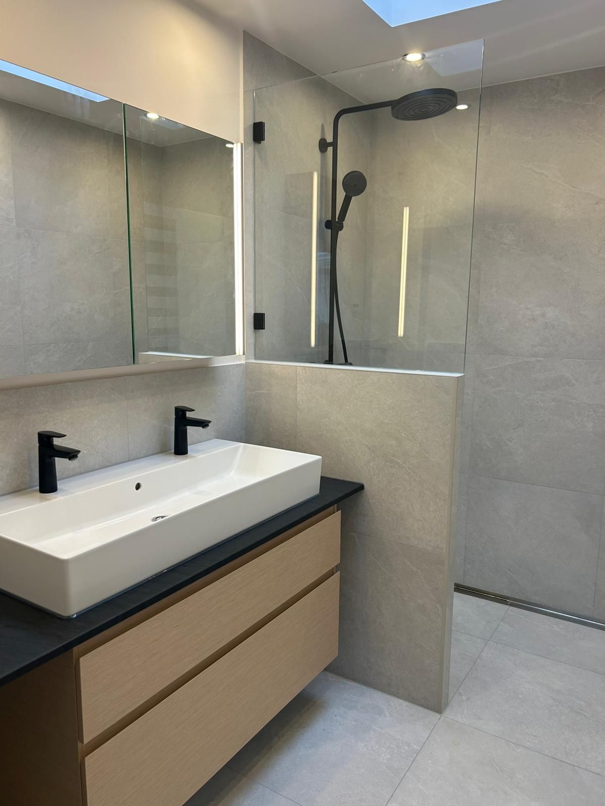 Modernes Badezimmer mit beigem Waschtisch, rechteckigem Waschbecken, schwarzen Wasserhähnen und Duschkabine aus Glas.