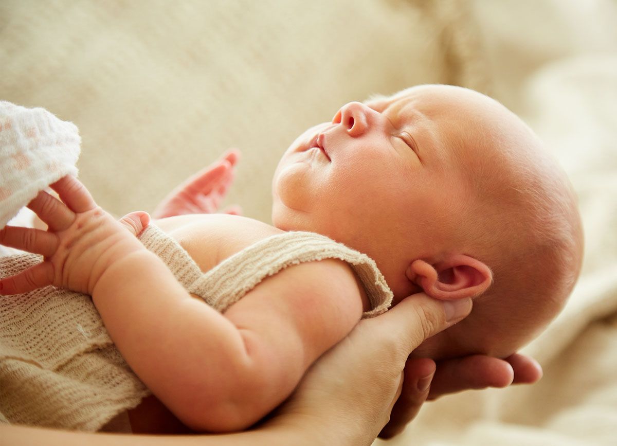 Neugeborenes Baby, sanft in den Händen gehalten, schläft mit geschlossenen Augen.