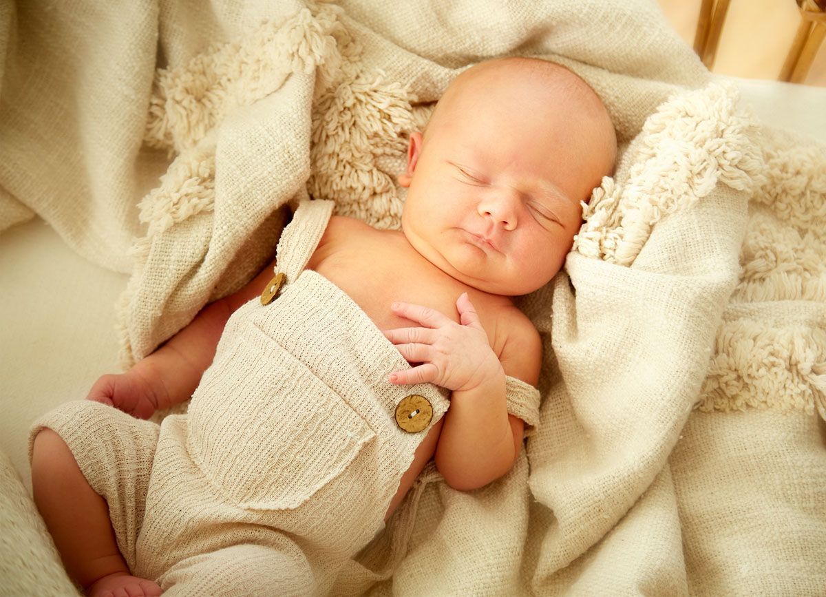 Neugeborenes Baby schläft friedlich in einer weichen, beigen Decke und trägt einen cremefarbenen Overall.