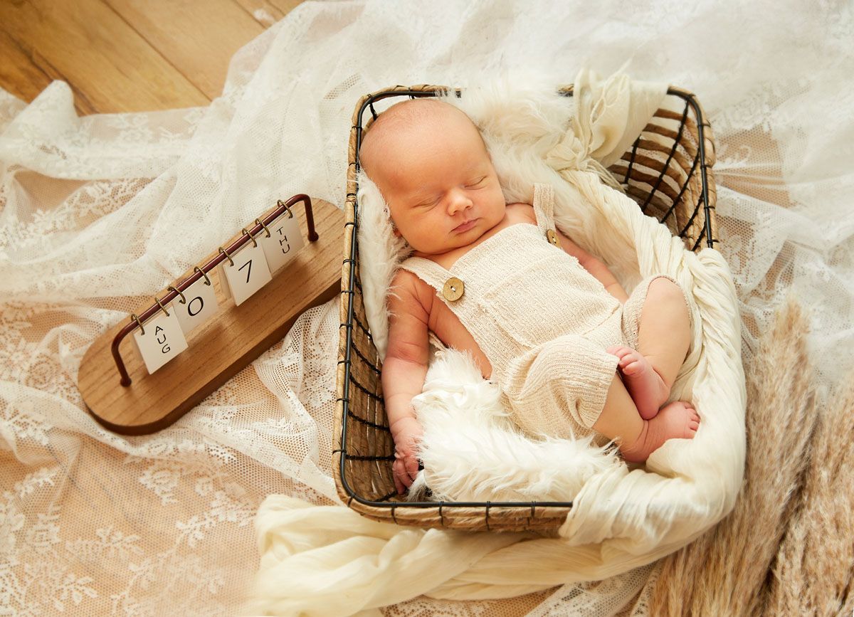 Neugeborenes Baby schläft in einem Weidenkorb, trägt einen cremefarbenen Strampler und liegt auf einer flauschigen Decke.