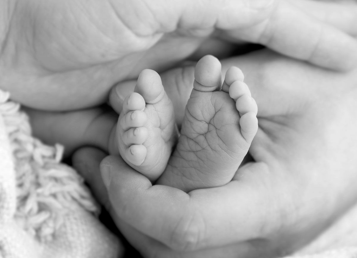 Erwachsene Hände wiegen winzige Füße eines Neugeborenen in Schwarz und Weiß.
