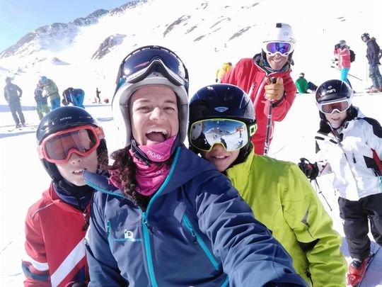 Grupo de esquiadores posando en una montaña nevada, sonriendo con ropa de esquí colorida y gafas.