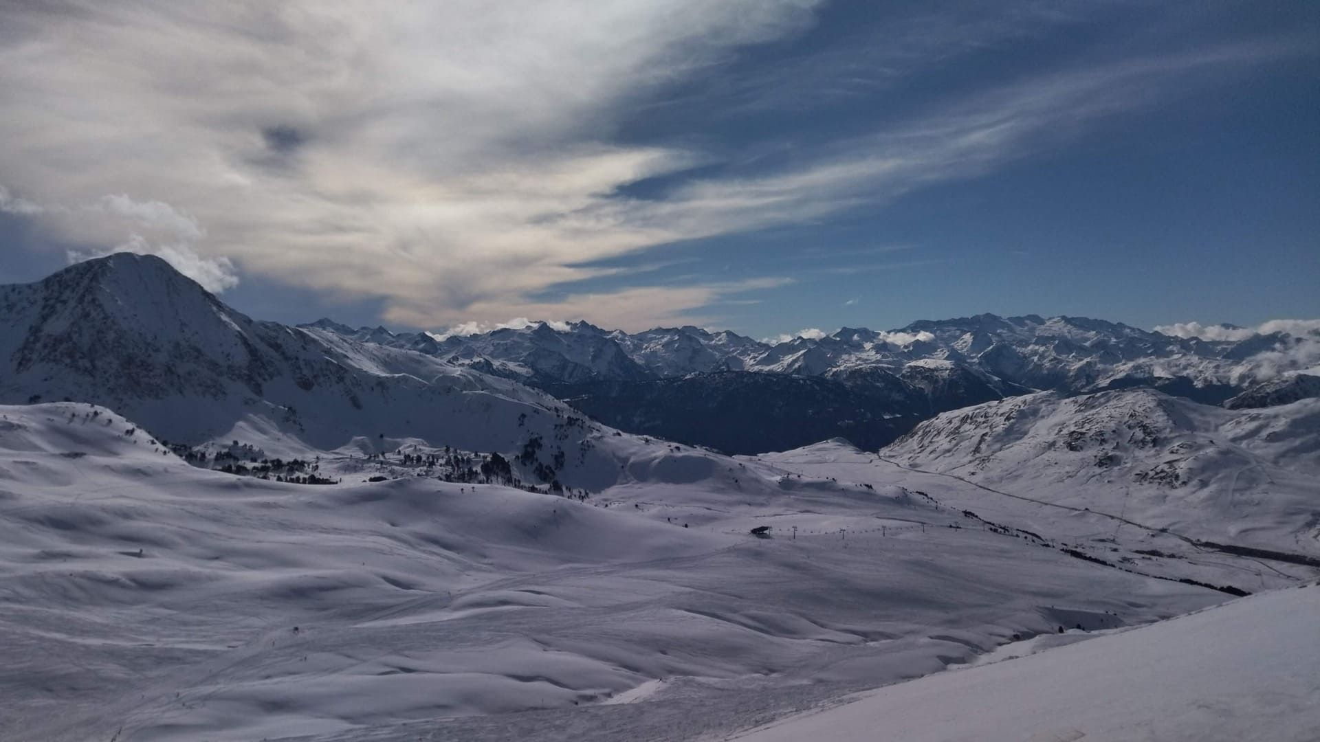 Cordillera nevada bajo un cielo nublado, con un amplio valle invernal en primer plano