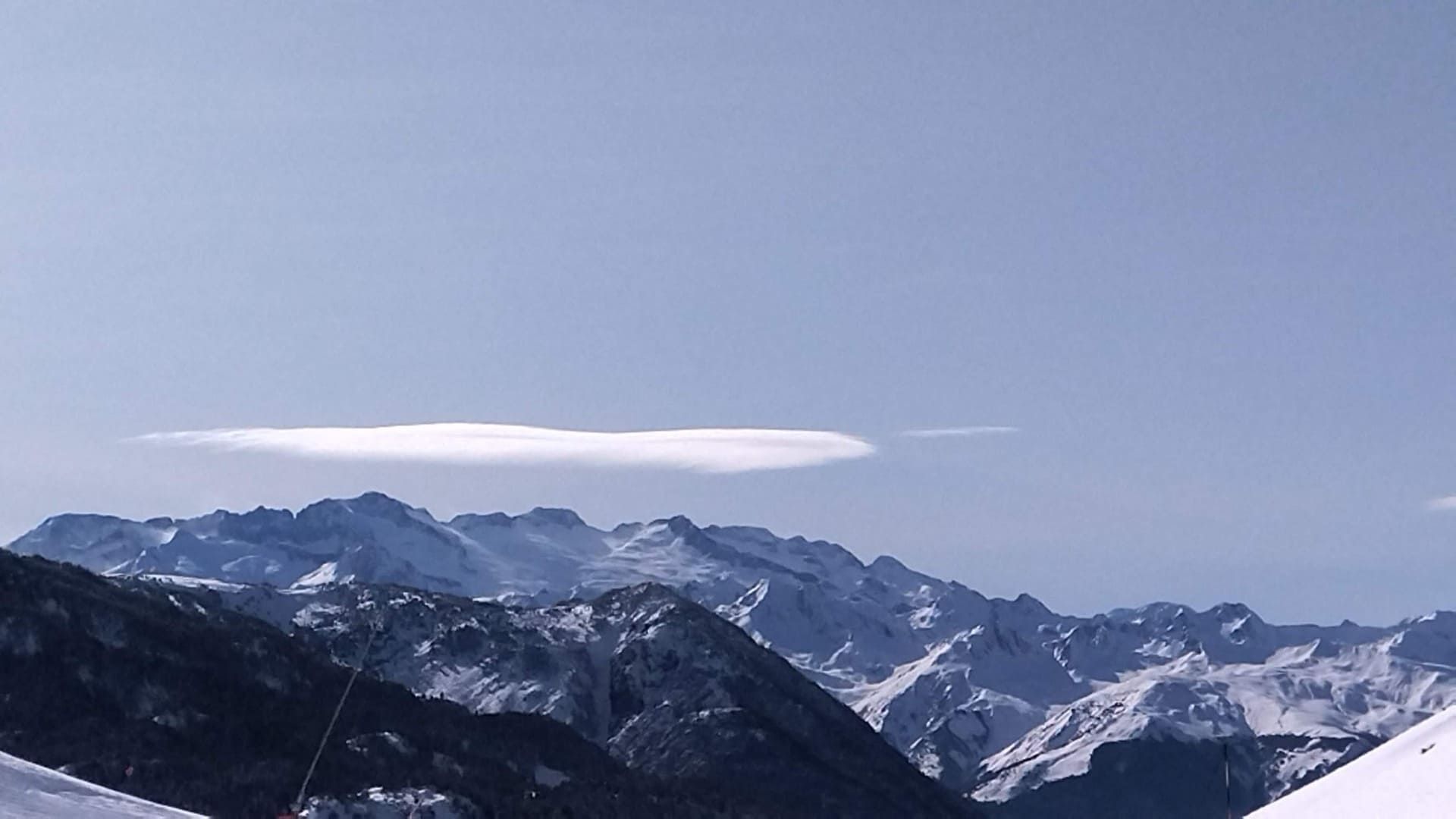Cordillera nevada bajo un cielo azul despejado con una nube larga y fina
