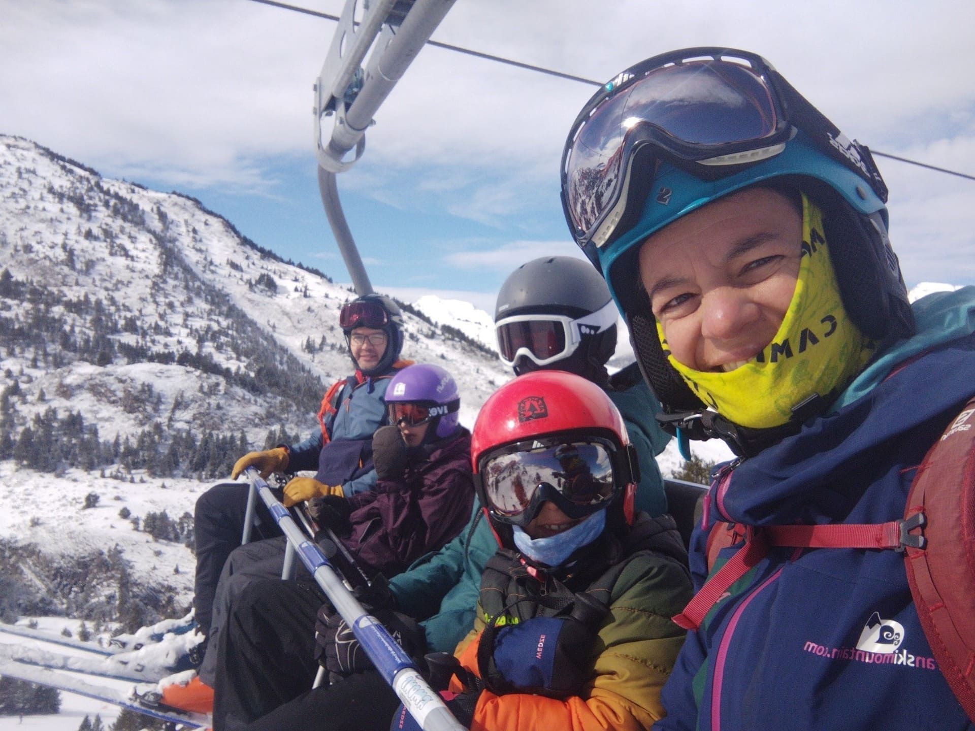 Selfi en un telesilla de cuatro esquiadores bien abrigados que sonríen en una montaña nevada, con gafas de esquí y cascos puestos.