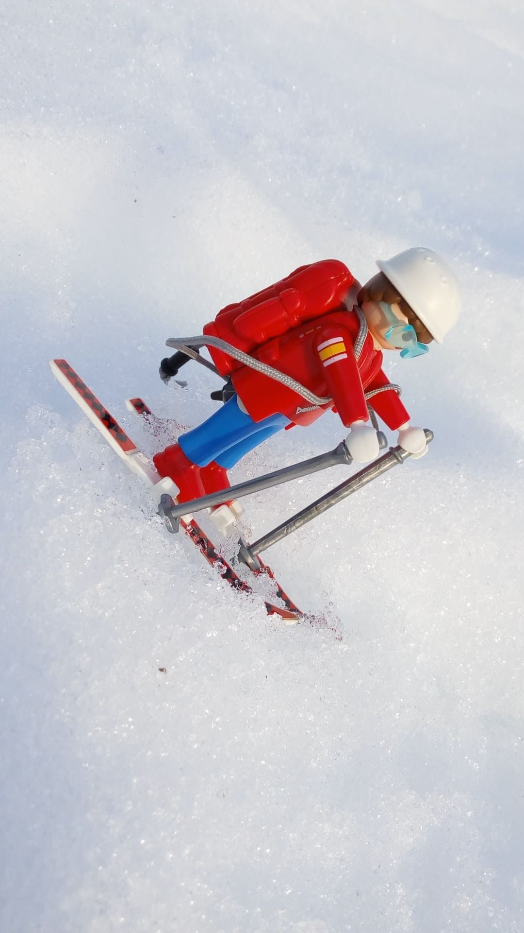 Niño con mono de nieve rojo esquiando cuesta abajo con casco y bastones