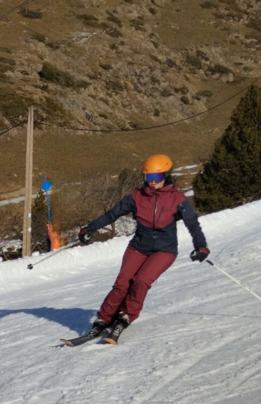 Esquiador con casco naranja y traje granate bajando una pendiente nevada haciendo giros