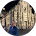 Persona de pie junto a un edificio de piedra con ventanas arqueadas y una gran pancarta, con una chaqueta azul