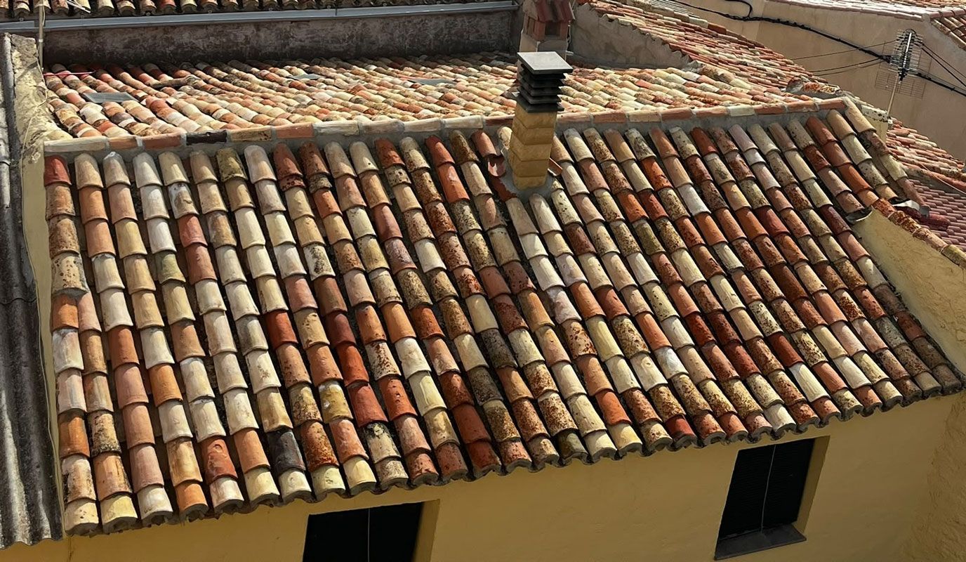 Un tejado de tejas con baldosas de arcilla rojas y marrones desgastadas por el tiempo y una chimenea.