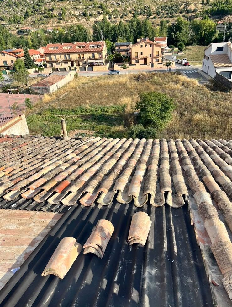 Vista desde la azotea sobre tejados de tejas y chapa ondulada hacia casas en la ladera y pastizales secos.