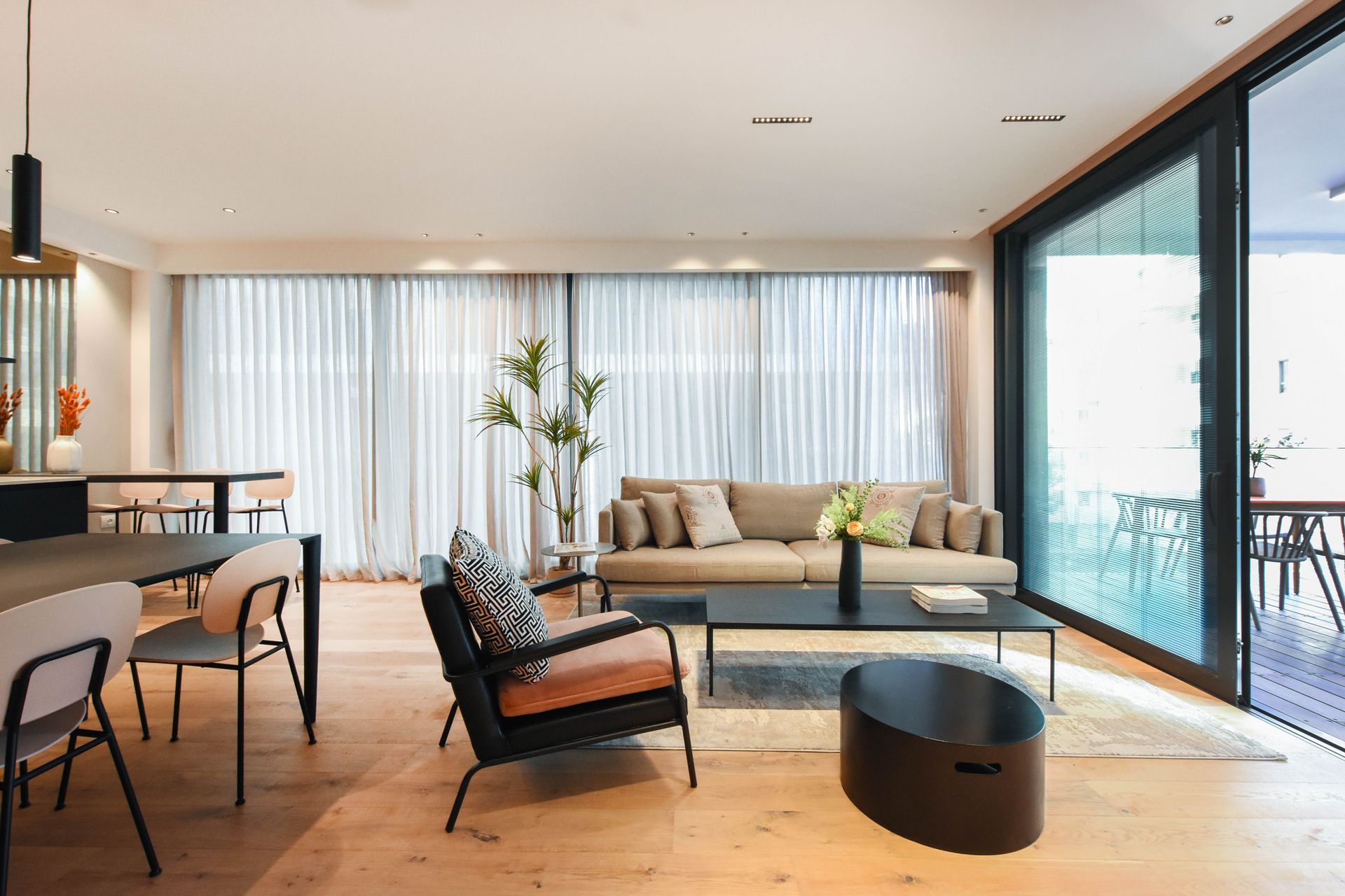Modern living room with tan sofa, black chair, sliding glass door, and dining area.