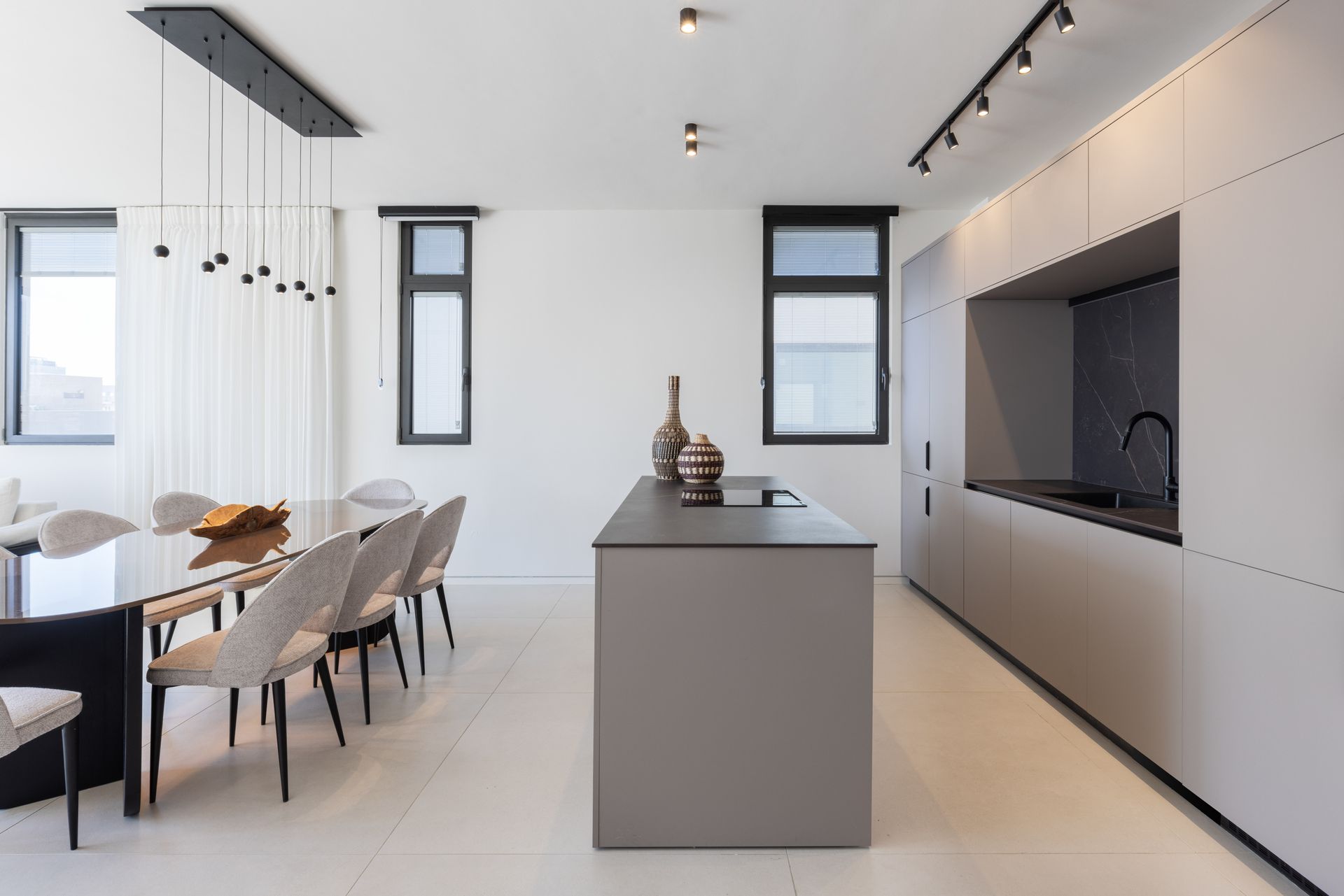 Modern kitchen with gray island, cabinets, dining table with chairs, and white walls.