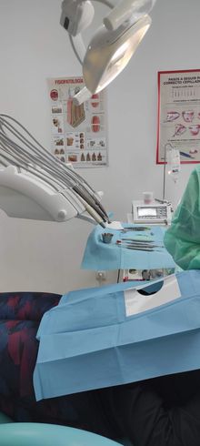Interior del consultorio del dentista, paciente en silla, paño azul, luz de techo, herramientas dentales y gráficos en la pared.