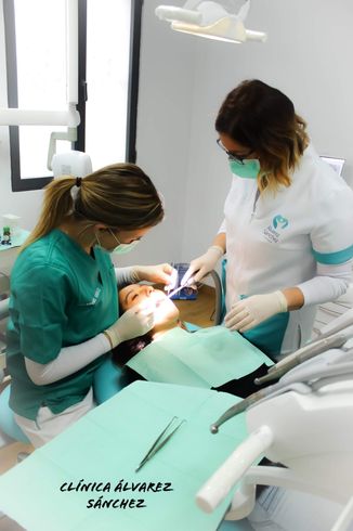 Dos dentistas con uniformes verdes y blancos atendiendo a un paciente en una clínica dental.