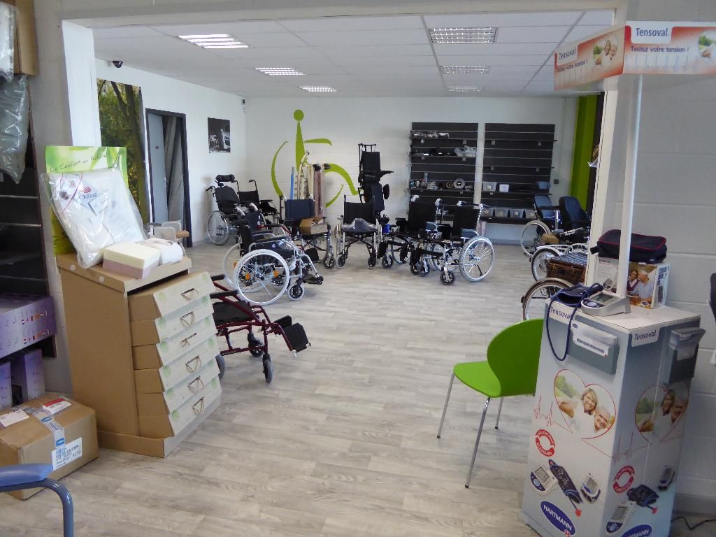 Magasin de fournitures médicales, plusieurs fauteuils et dispositifs sont exposés sur un sol clair imitant le bois.