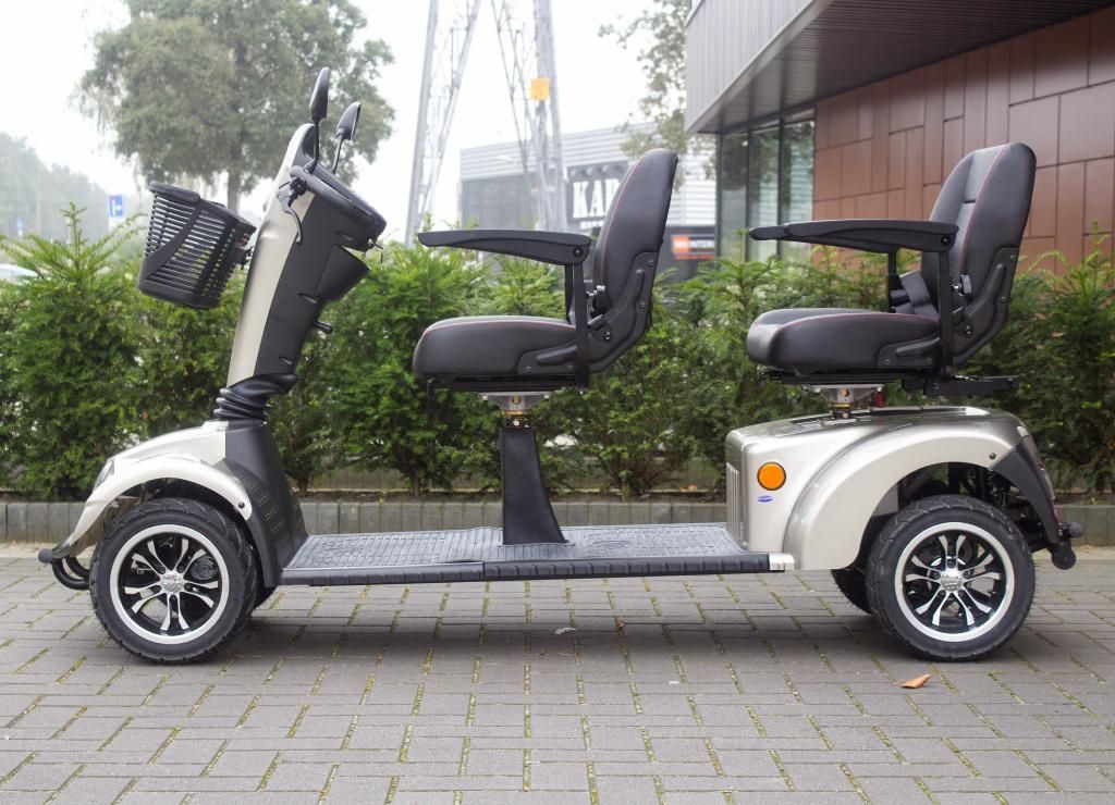 Scooter de mobilité biplace, argent métallisé et noir, stationné sur des pavés.