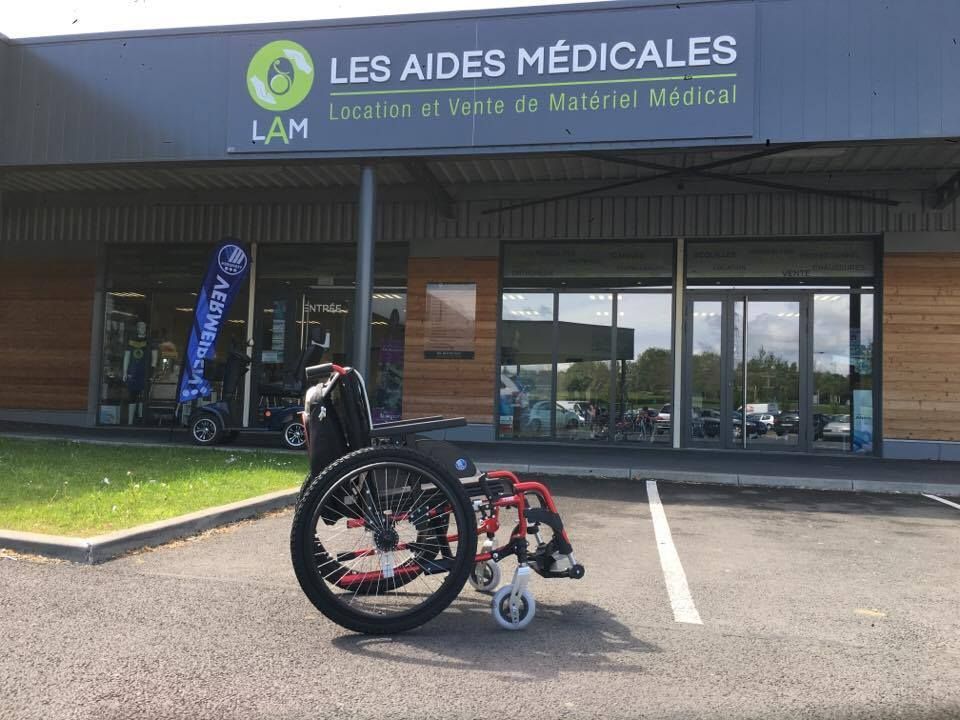Un fauteuil devant le magasin de fournitures médicales Les Aides Médicales. La façade du magasin est dotée de vitrines.