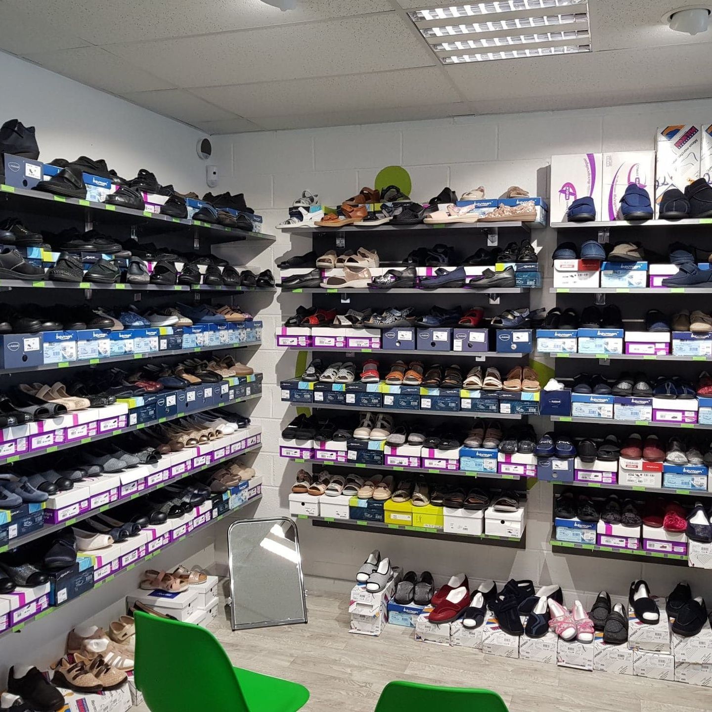 Intérieur d'un magasin de chaussures avec des étagères à chaussures, un miroir et des chaises vertes.