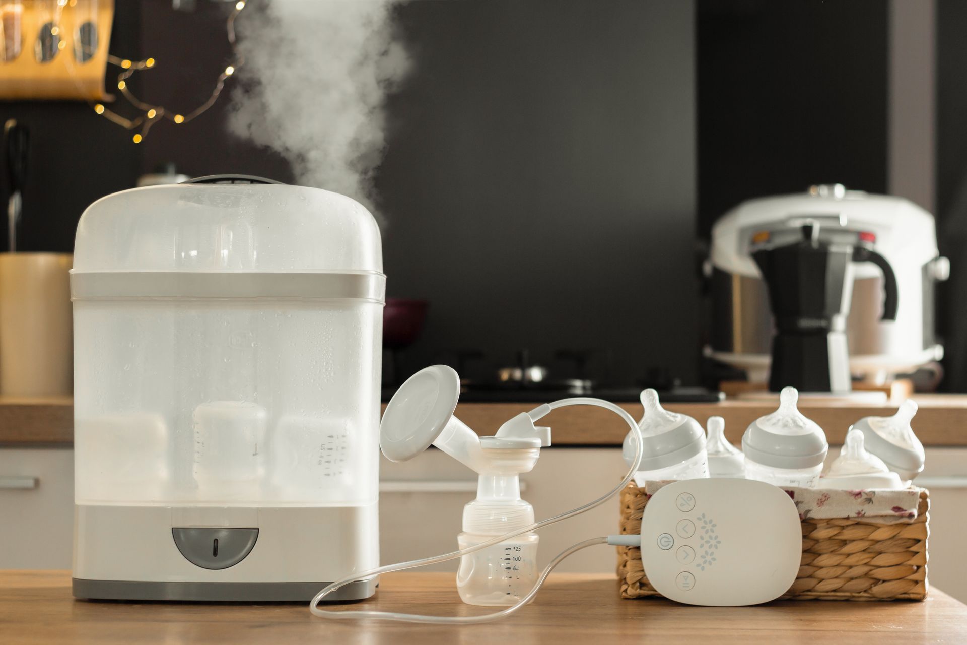 Stérilisateur à vapeur pour biberons et tire-lait avec biberons et accessoires sur un plan de travail dans une cuisine.