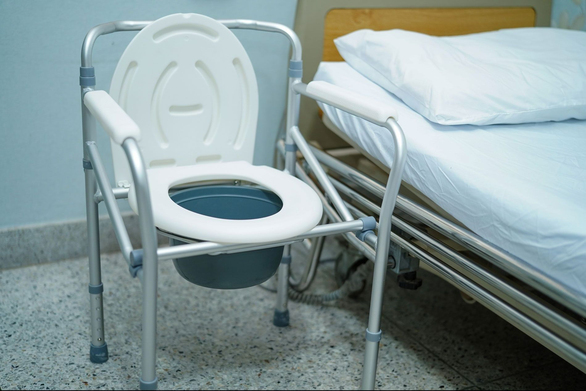 Chaise percée de chevet près d'un lit dans une chambre d'hôpital.