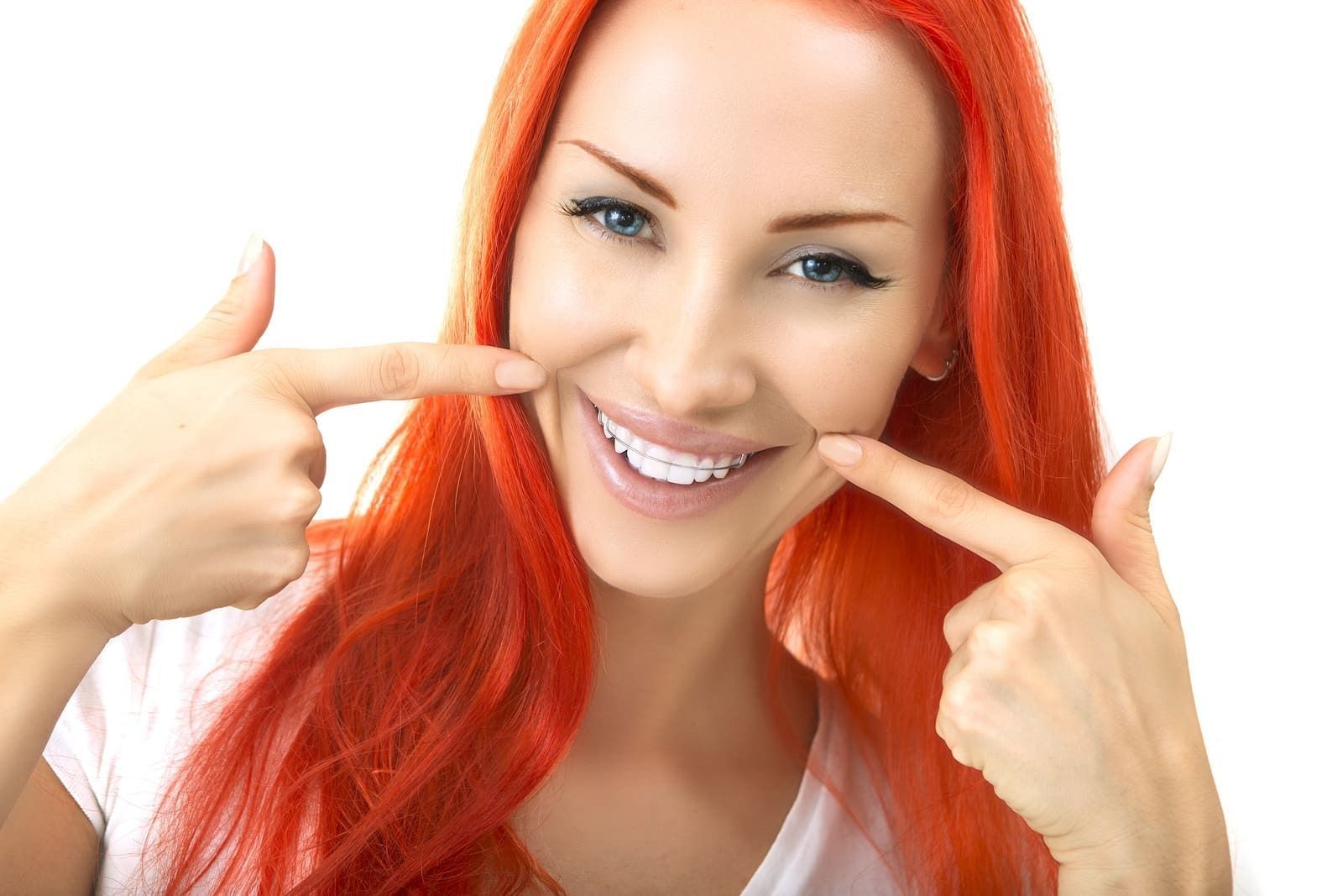 Una mujer con cabello rojo sonríe y señala sus dientes.